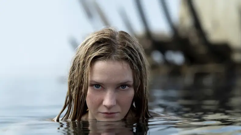 An image of Morfydd Clark as Galadriel, seen in the water in front of a shipwreck.