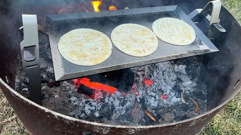 Three flour tortillas browning on top of Made In Carbon Steel Griddle cooktop.