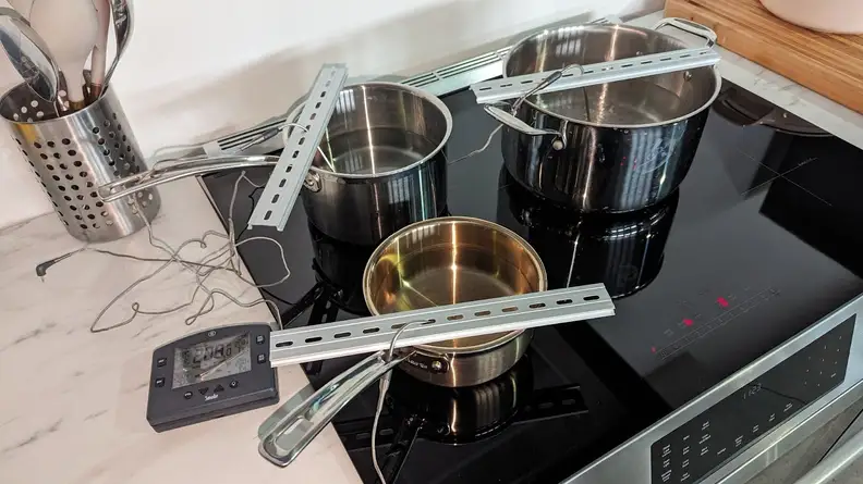 Three small pots with temperature readers inside on cooktop of the Bosch HII8057U 800 Series Induction Slide-in Range.