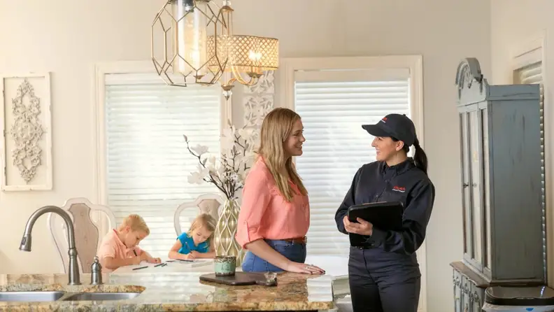 Pest control technician speaking with homeowner in kitchen with children