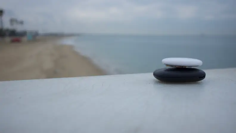 An Apple AirTag stacked on top of a Galaxy Air Tag, overlooking the beach.