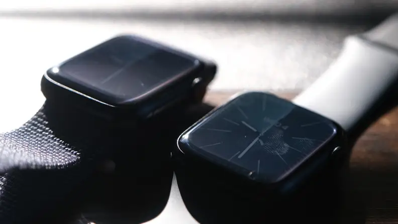 Two Apple smartwatches side by side on top of wooden surface on a sunny day.