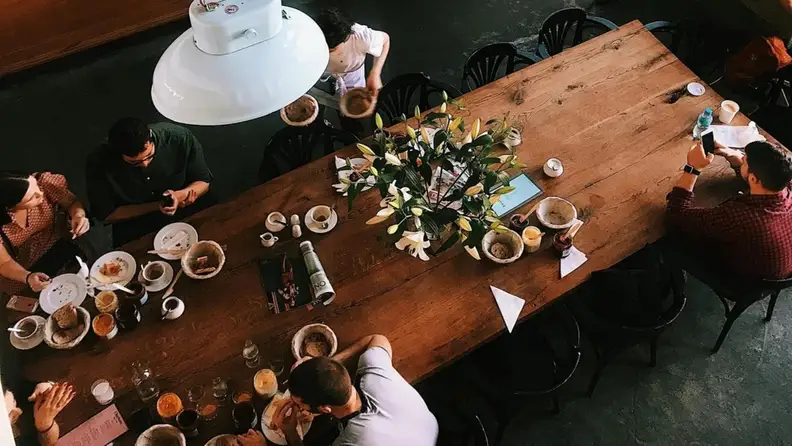 Aerial view of people seated at a long table with coffee