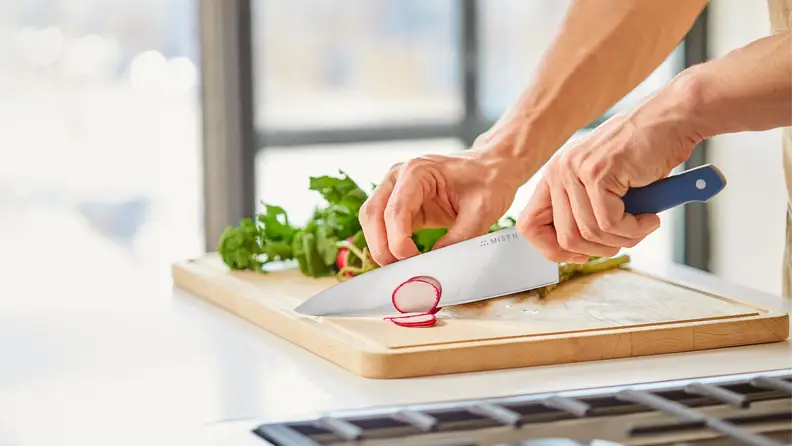 A cook uses a sharp kitchen knife to slice radishes on a cutting board while prepping fresh produce for HelloFresh meals.