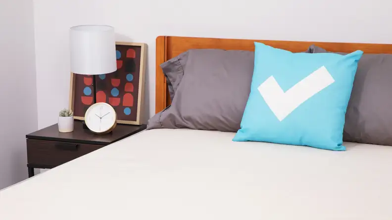 A Nolah Natural mattress inside of wooden bed frame with pillows on top next to nightstand table.