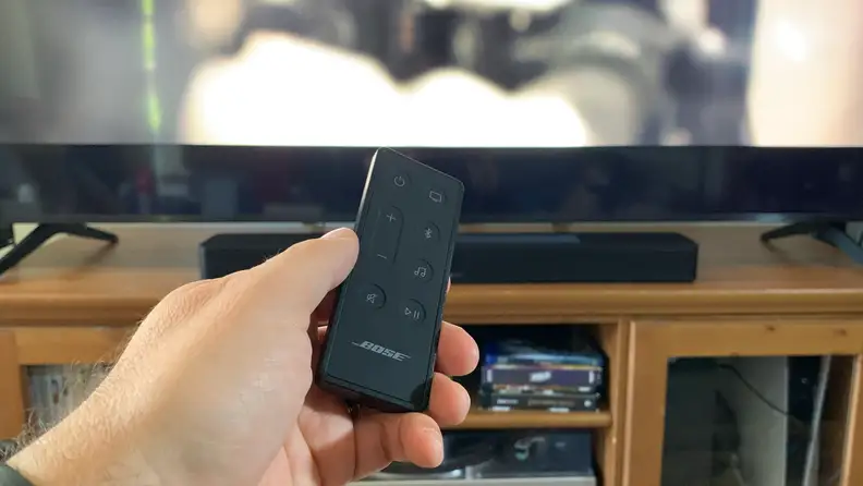 A hand holding the remote for the Bose Smart Soundbar 600.