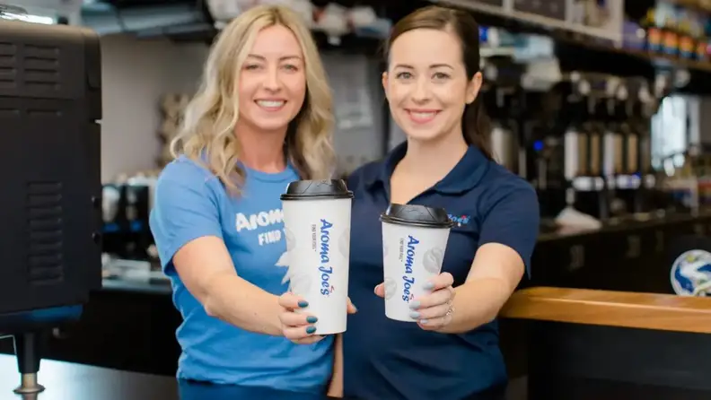 Two smiling baristas holding Aroma Joe's coffee cups