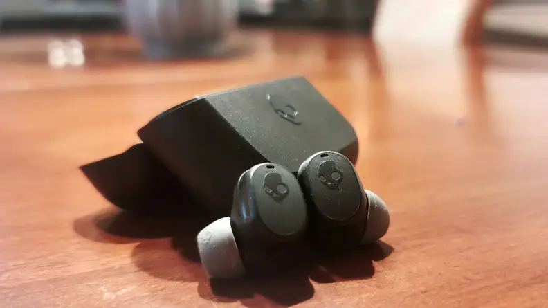 Skullcandy Mod XT earbuds in black sit on a wooden cabinet.