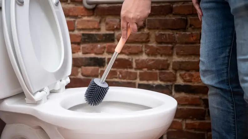 A person cleans a toilet with a toilet brush