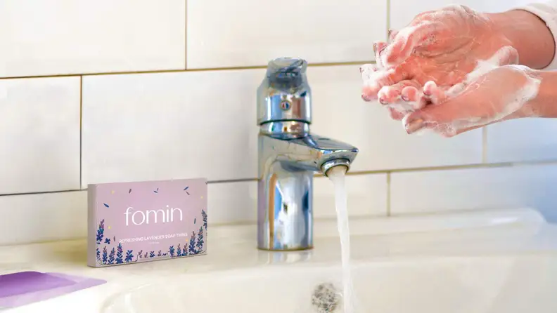 The Fomin hand soap sheets on a sink shelf next to a person washing their hands