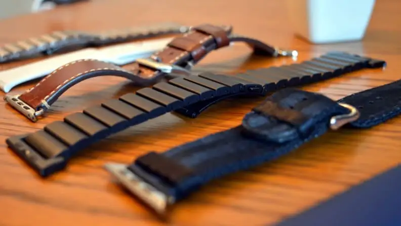 Five different Apple watch bands, like leather, rubber, and and velcro ones, sitting on top of a wooden table.