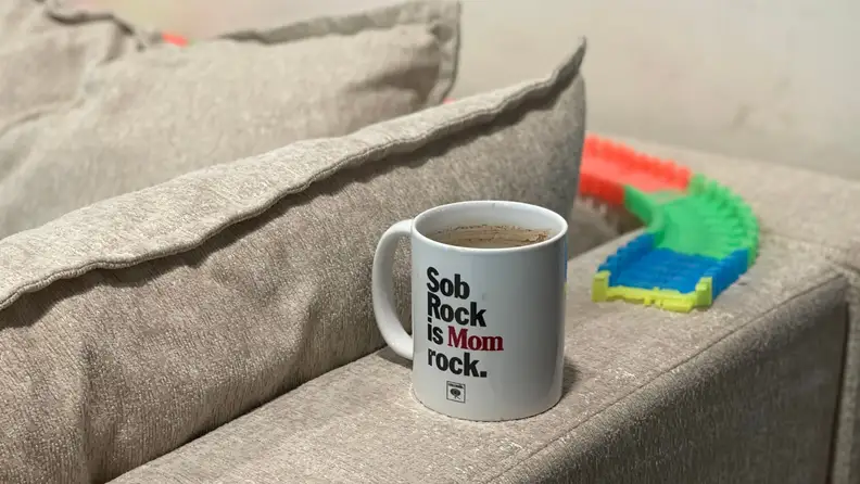 A coffee mug and kids toy car tracks on the arms and back of the Kova Sofa