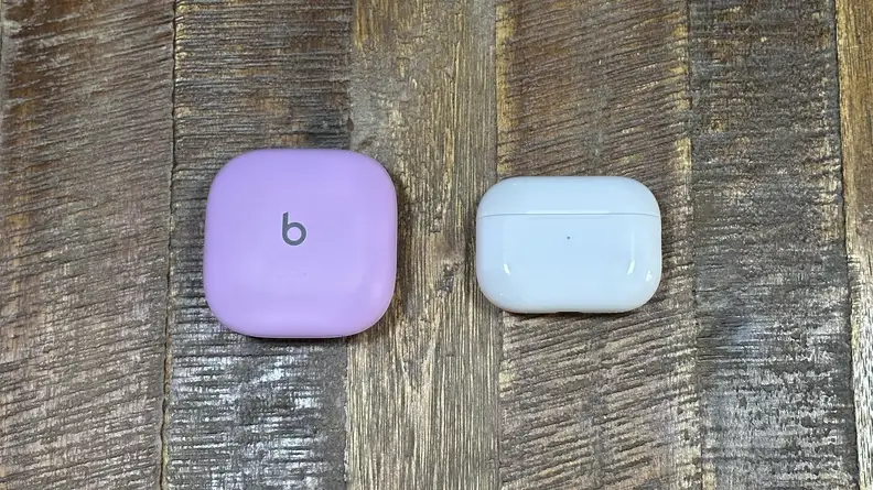 The purple Beats Fit Pro and white AirPods Pro 2 case next to one another on a wooden table.