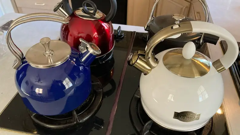 Four tea kettles sit on four stovetop burners.