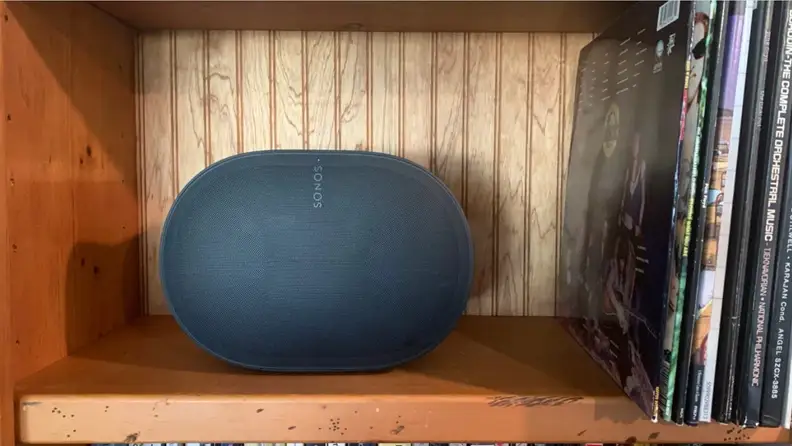 The Sonos Era 300 on a wooden bookshelf with records leaning next to it.
