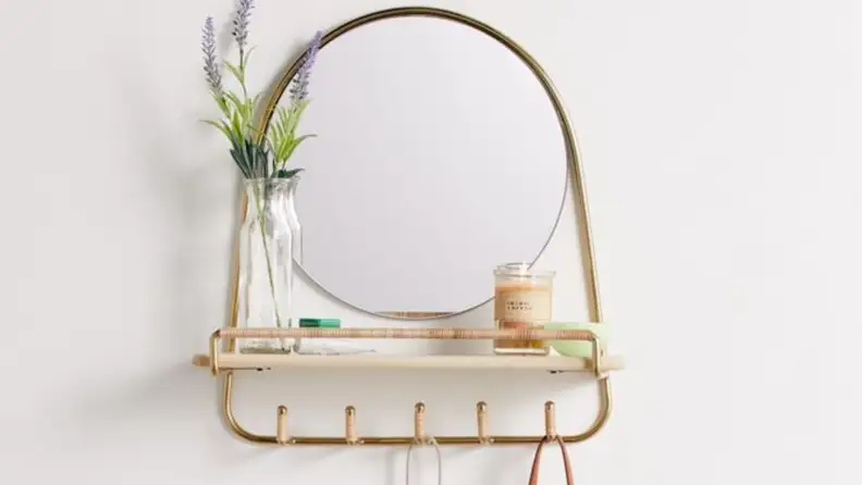 Gold oval-shaped mirror with a shelf and hooks on a white wall