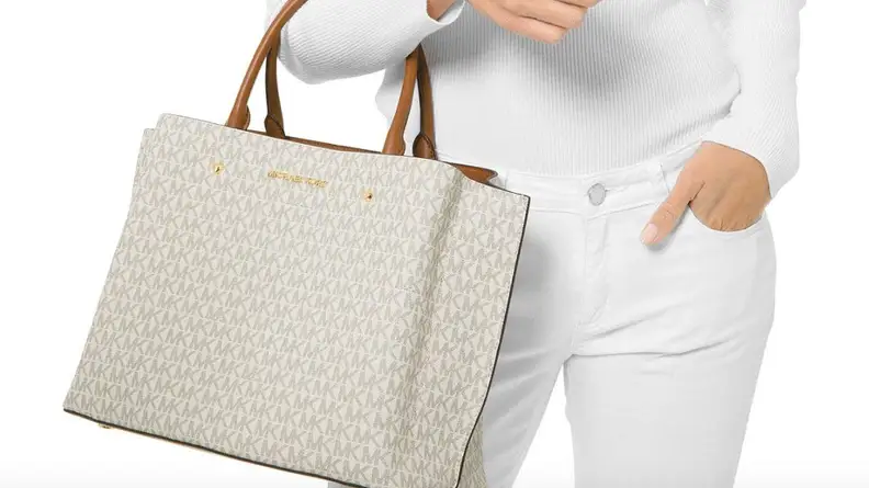 A woman in white holding a white Michael Kors bag.