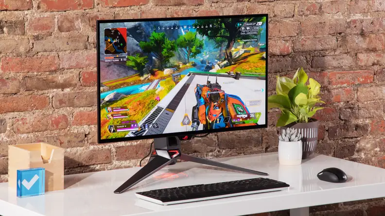 Asus ROG Swift OLED PG27AQDM desktop computer on top on desk in front of brick wall.