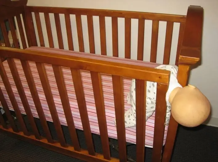 A drop sided crib with a doll caught in the opening to demonstrate potential dangers and injuries.