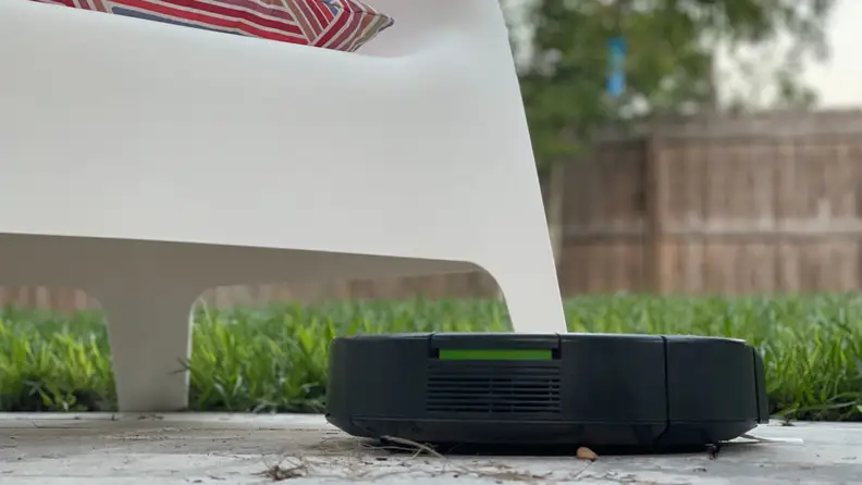 An iRobot vacuum on a patio with a chair in the background.
