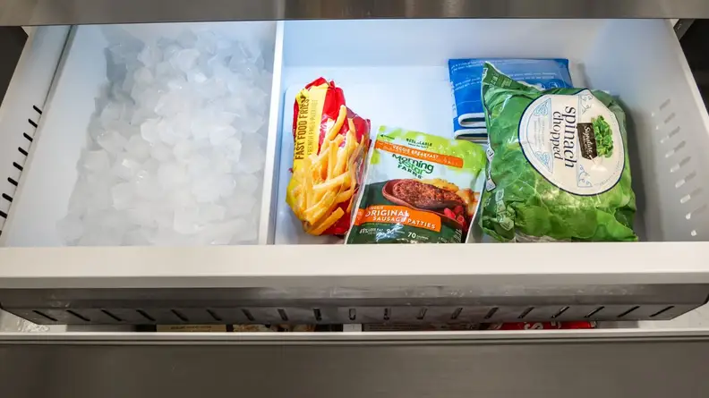 Assorted bags of frozen foods inside of freezer drawer next to ice tray.