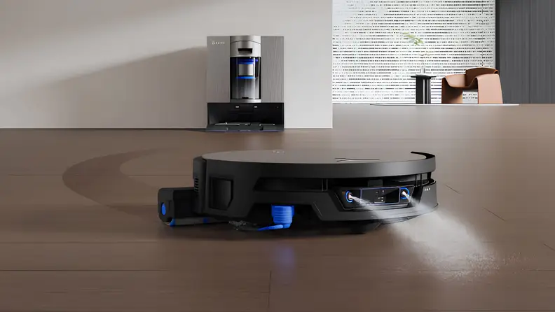 The Ecovacs Deebot X12S OmniCyclone robot vacuum cleaning a hardwood floor, with its base station in the background.