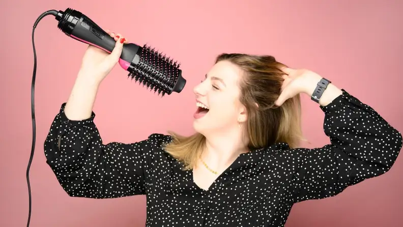 A woman "singing" into a Revlon One-Step Hair Dryer Brush as though it were a microphone