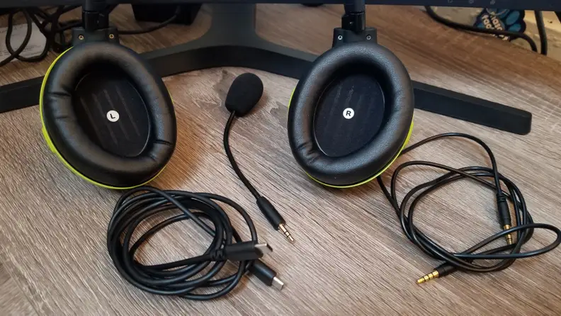 Various pieces and cords from an audio headset are laid out on a desk: a charger, audio cable, mouthpiece, and earphones.