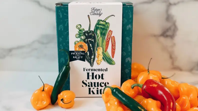 A Farm Steady hot sauce making kit sits on a marble surface surrounded by various citrus and peppers.