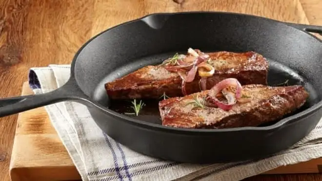 Slabs of seasoned meat cook inside a cast-iron skillet.