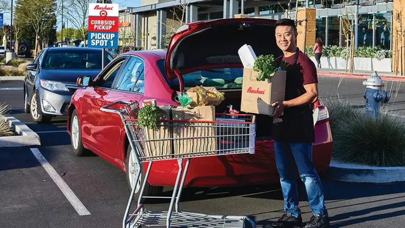 Employee loading curbside pickup groceries into a car trunk