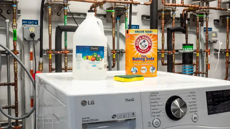 A jug of vinegar, a box of baking soda, and a sponge on a washing machine