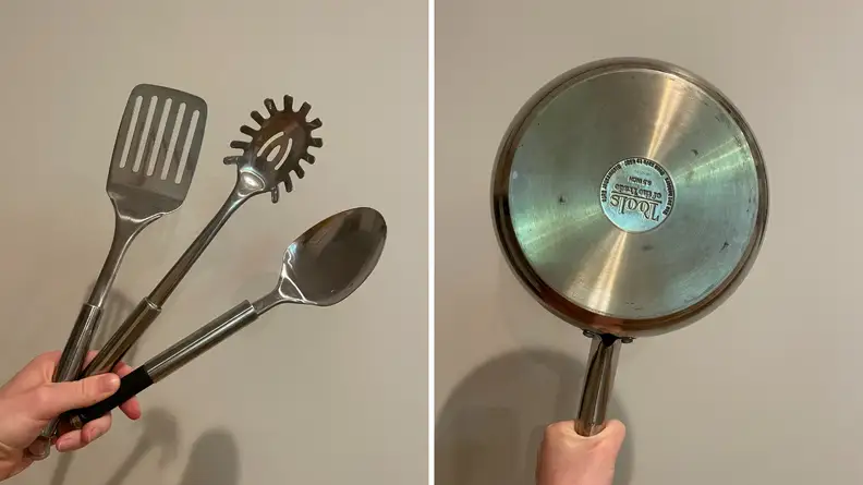 On the left, a hand holding a stainless steel spatula, spoon, and pasta server. On the right, the bottom of a stainless steel frying pan.
