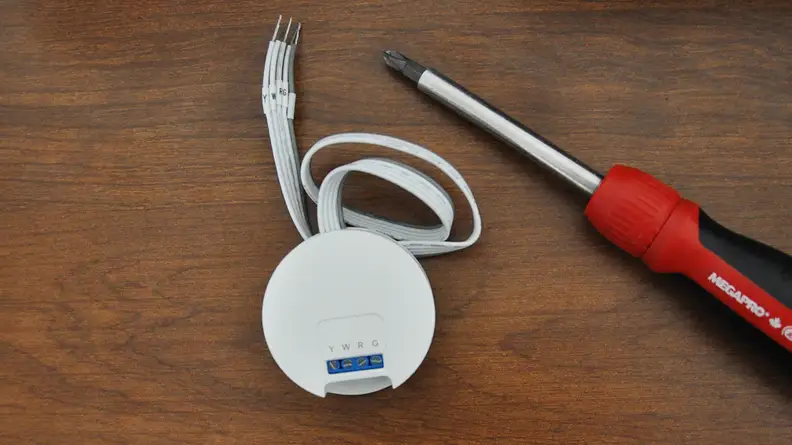 Interior piece of thermostat, cable, and screwdriver on wood tabletop.