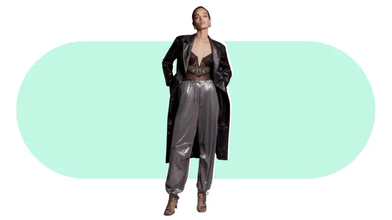 A model wearing silver pants with a corset top and long coat.
