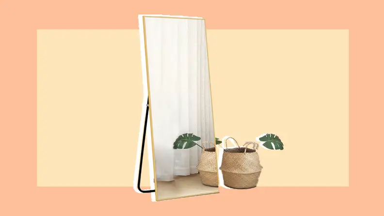 Freestanding rectangle-shaped mirror wall next to straw bin and palm frond.