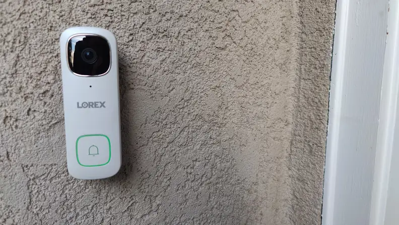 White Lorex 2K Wired Video Doorbell mounted on wall on home outdoors.
