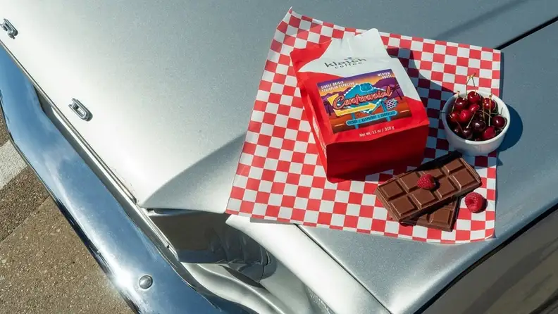 Klatch Coffee Centennial bag on a checkered paper with cherries and chocolate on a car hood