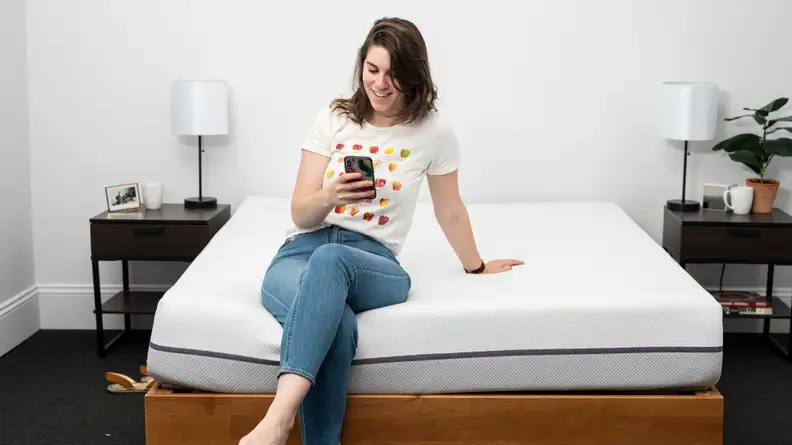 a person sits on the end of the Purple mattress on their phone