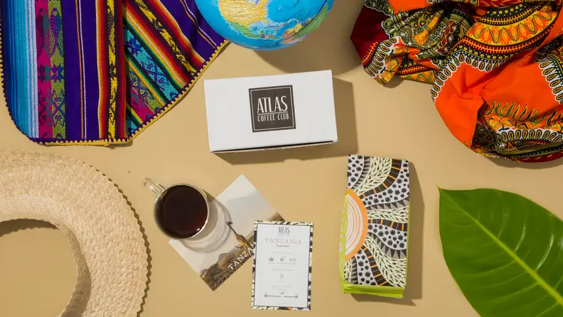Atlas Coffee Club box with a Tanzania coffee bag, postcard and cup on a tan surface
