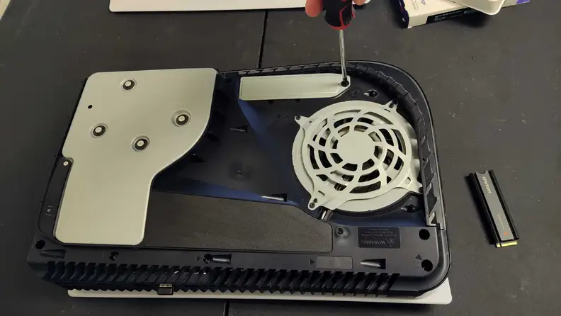 The Sony Playstation 5 uncovered with the cooling fan on display and a screwdriver untwisting open the expansion slot.