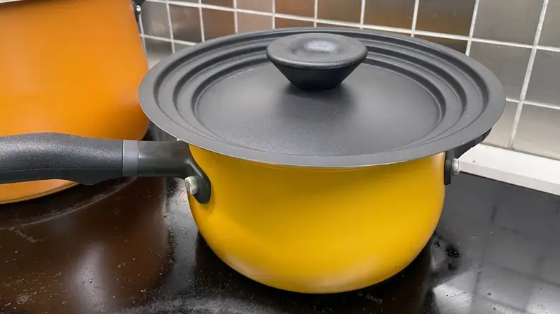 Small yellow pot with black lid sits on top of cooktop.