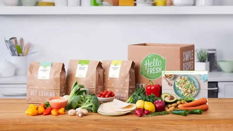 An unpacked box of a meal delivery kit with various ingredients, is laid out on a kitchen counter.