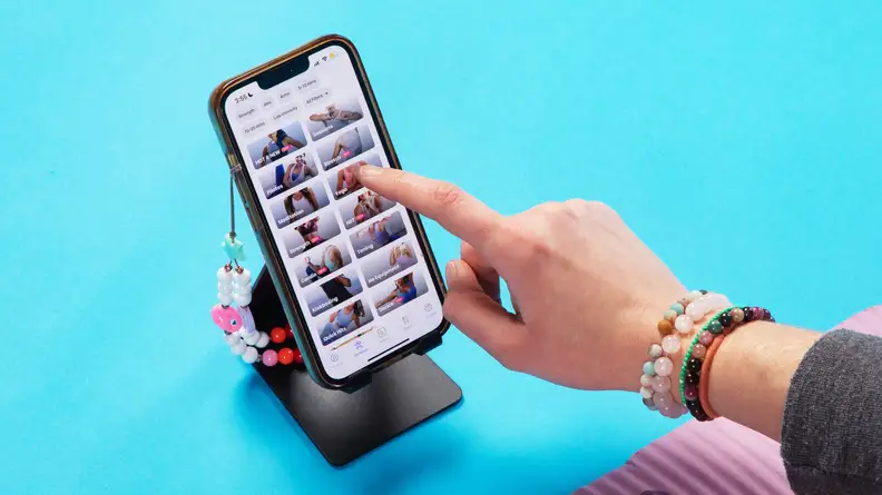 Person using finger to navigate the FitOn fitness app on smart phone.