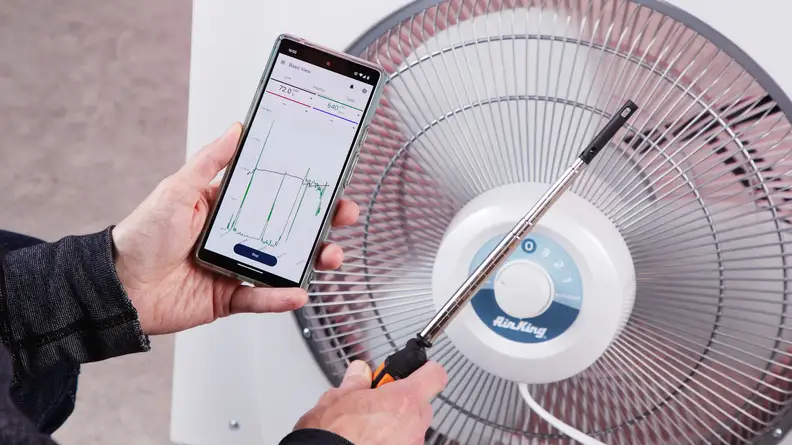 A close-up of someone holding a smart anemometer up to a fan.