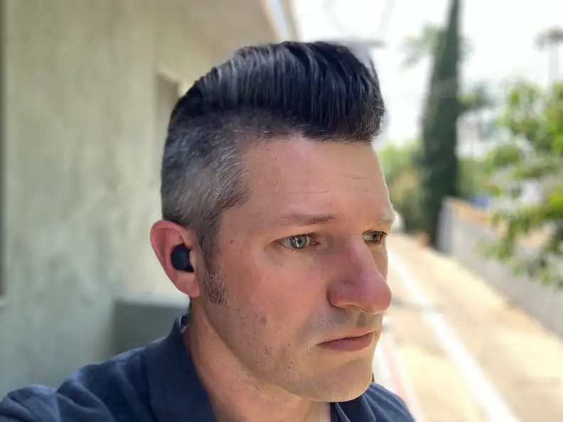 A man in a blue shirt listens to the black Sony LinkBuds S while standing on a balcony.