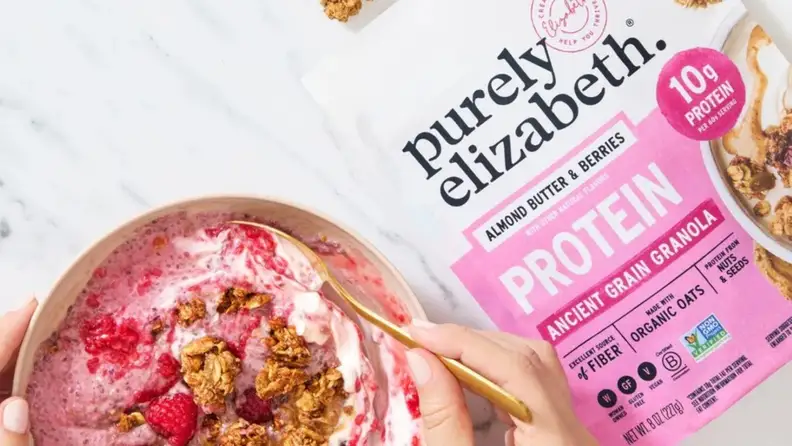 Purely Elizabeth protein granola bag beside a bowl of yogurt and berries