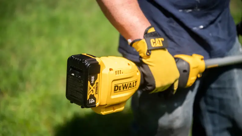 A man holds a weed wacker with a battery pack at one end