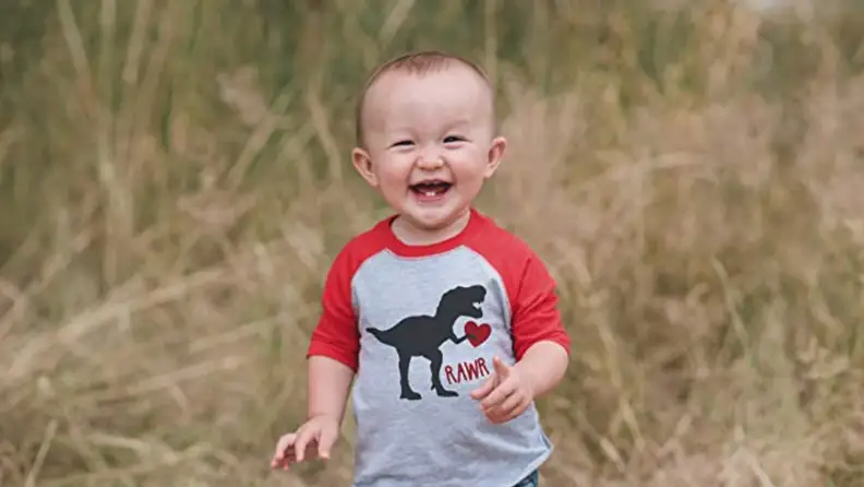 Child smiling wearing gray and red with dinosaur on front.