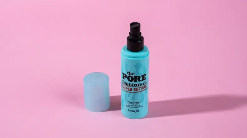 A turquoise bottle of makeup setting spray on a pink background.